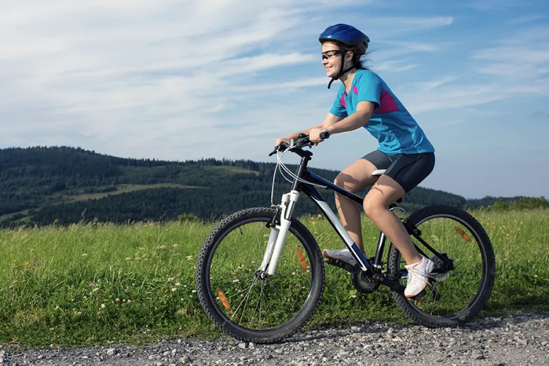 Man wearing helmet rides bicycle past grassy, hilly landscape