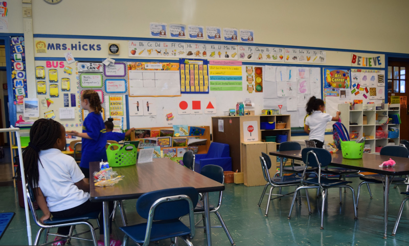 Three children sit and stand inside elementary school classroom