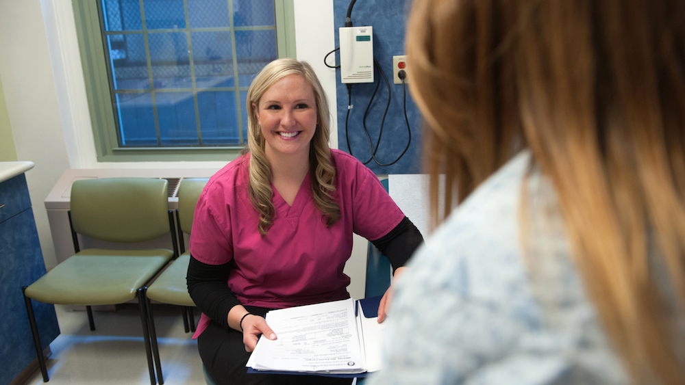 Smiling clinician holding papers speaks with patient who has back to camera