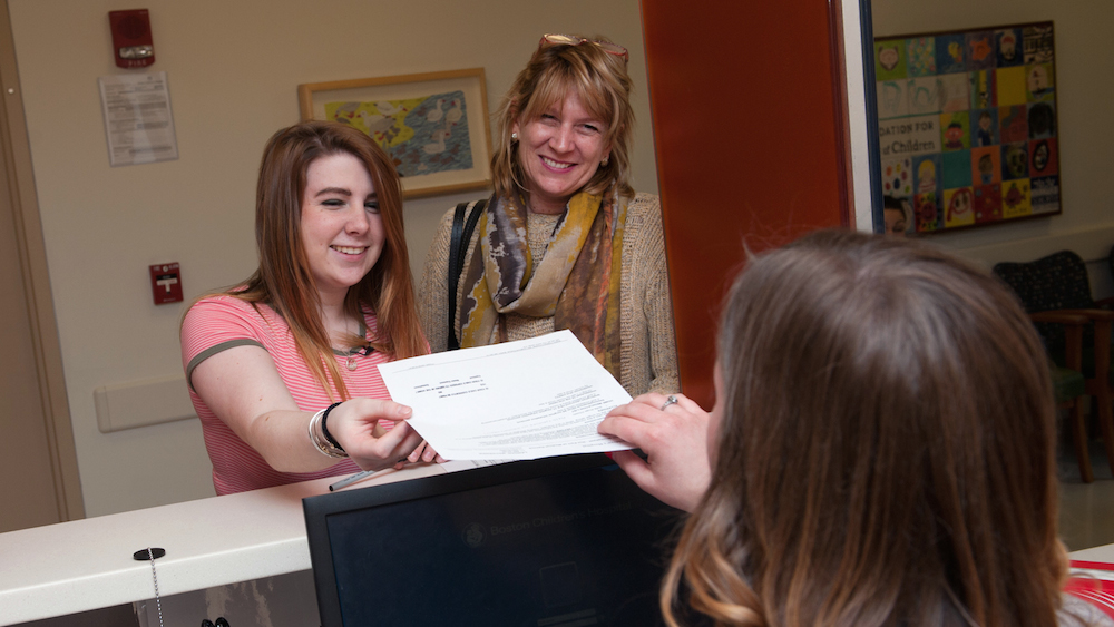 Receptionist hands paperwork to teenage female accompanied by adult woman