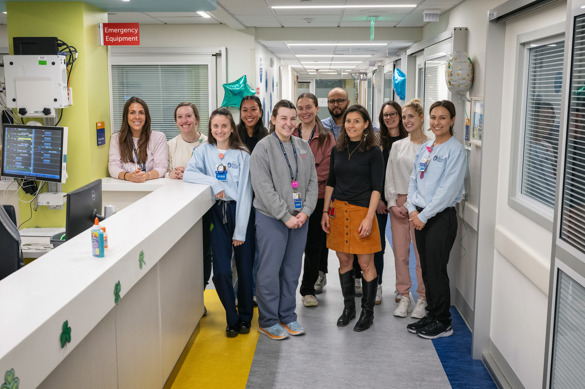 11 people (10 women, 1 man) pose for photo in hospital ward corridor