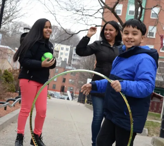 Three children pose for camera. Boy at front holds a hula hoop.