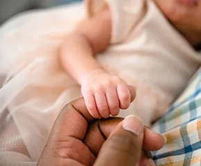 Baby's tiny right hand grasps an adult's finger