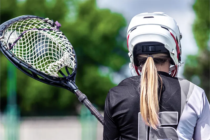 Girls' lacrosse player with ponytail holding stick and cradling ball, viewed from back