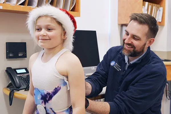 Male clinician secures back brace on young child wearing a Santa Claus hat