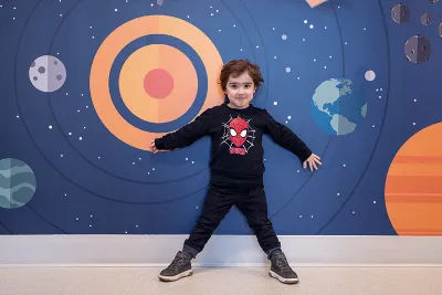 Boy stands in front of vibrant wall, with arms and legs spread out in a star-like shape