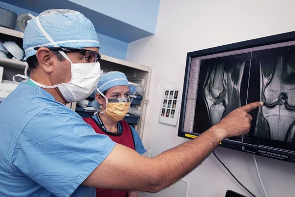 Two physicians study an image of the bones and ligaments of the knee.