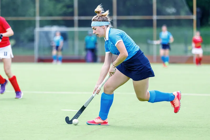 Players carries ball on stick up field hockey field