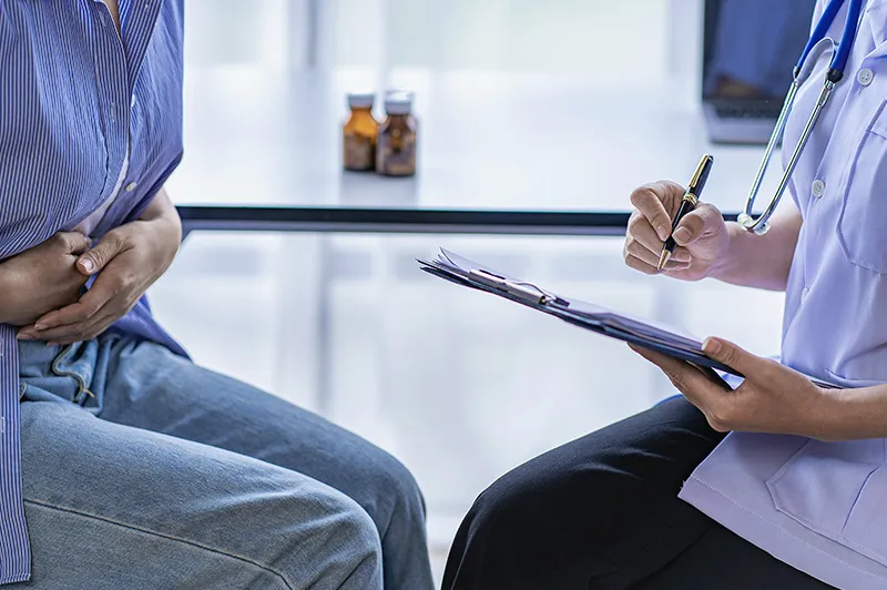 Patient sitting at left clutches abdomen; clinician on right holds clipboard in left hand and pen in right hand