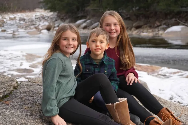2 girl and 1 boy siblings sit on rock near river