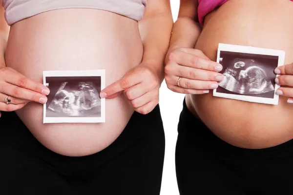 Pregnant women hold ultrasound images against bellies