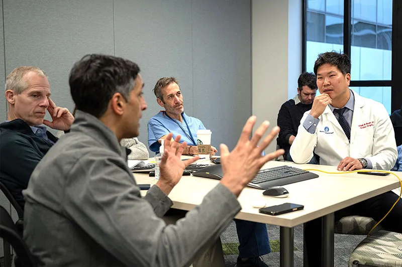 Man speaks and makes hand gestures while speaking with others in conference room