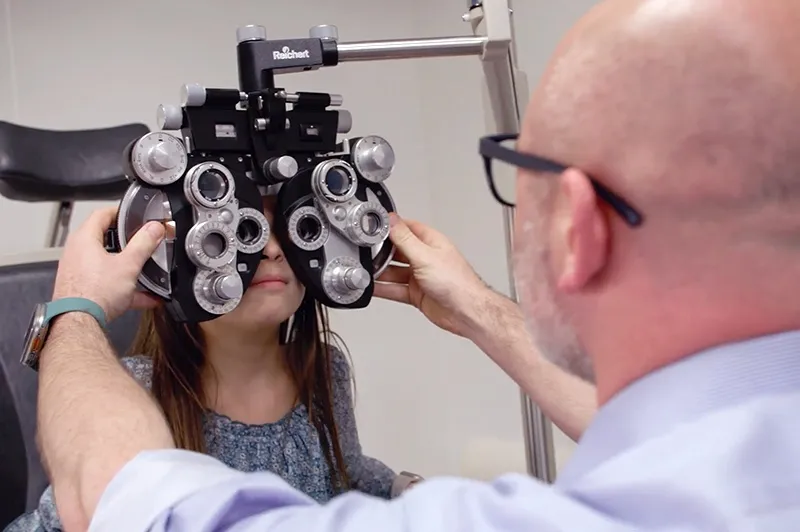man holding eye exam machine in front of young girl