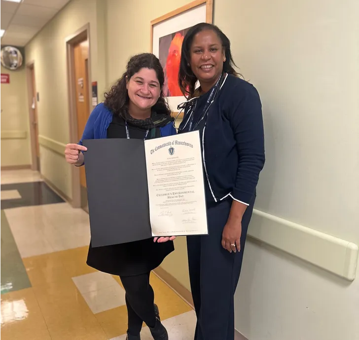Two women stand in a hallway holding a copy of a formal resolution
