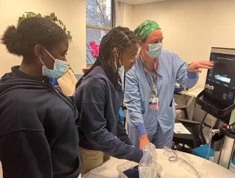 two girl interns and a nurse in blue scrubs looking at a screen
