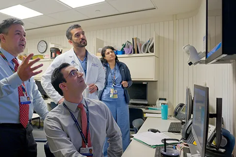 Four clinicians look at a computer monitor placed against a wall